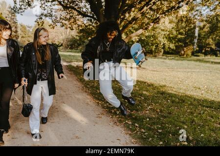 Une femme joyeuse sautant avec un skateboard tandis que des amies marchent à côté dans le parc Banque D'Images