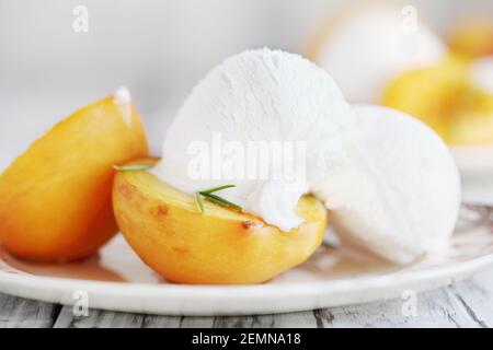 Pêches fraîches rôties maison cuites au sucre brun et aux branches de romarin frais et servies avec de la glace à la vanille. Mise au point sélective avec arrière-plan flou Banque D'Images