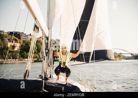 Femme sénior se carouchant en tenant la corde dans le bateau sous le soleil jour Banque D'Images