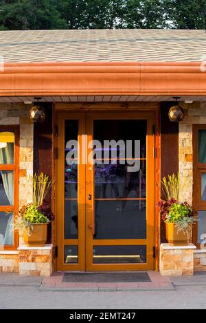 porte marron avec poignée et insert en verre la façade du bâtiment en carreaux de pierre avec fleur vases et une entrée avec un tapis de pied sous un can Banque D'Images