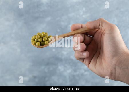 Homme tenant une cuillère olive avec la main sur fond gris Banque D'Images