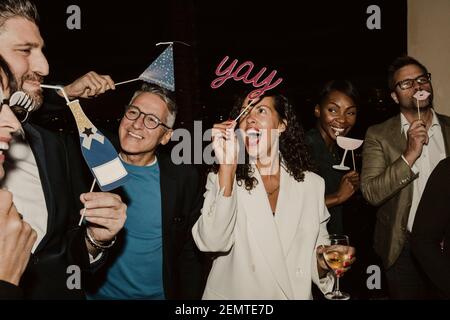 Des gens d'affaires joyeux appréciant avec des accessoires pendant la fête de l'entreprise à nuit Banque D'Images