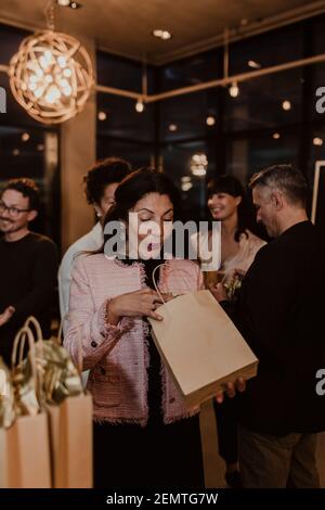 Surprise femme entrepreneur peeking dans sac cadeau pendant la fête à l'intérieur bureau Banque D'Images