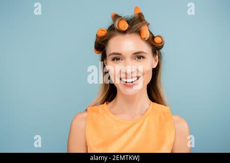 une femme joyeuse regardant l'appareil photo tout en utilisant des carottes au lieu de boucles isolées en bleu Banque D'Images