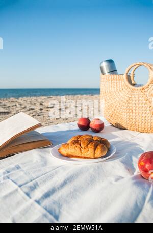Pique-nique agréable au bord de la mer avec croissants frais et livre ouvert prêt pour la lecture. Banque D'Images