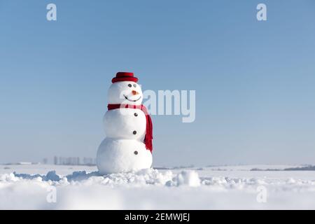 Bonhomme de neige amusant dans un élégant chapeau rouge et un scalf rouge sur un terrain enneigé. Ciel bleu sur fond Banque D'Images