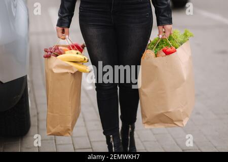 Produits d'épicerie d'un supermarché dans un forfait éco-artisanat. Livraison de nourriture pendant la quarantaine. Sacs écologiques en papier remplis d'aliments frais. La femme tient deux paquets par le Banque D'Images