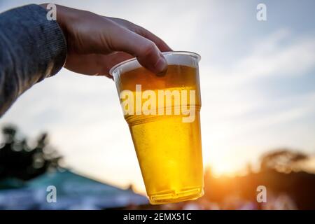 Verre de bière en plastique à la main au coucher du soleil. Banque D'Images
