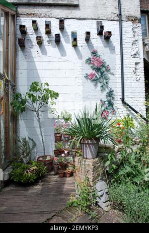 Coin de Dalston Eastern Curve Garden avec plantes en pot et boîtes à oiseaux contre mur peint en blanc, quartier de Hackney à Londres Banque D'Images