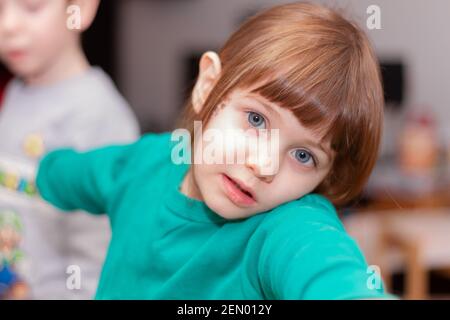 Portrait d'une petite fille en chandail vert dans une cuisine mignonne, à cheveux bruns, à yeux bleus Banque D'Images