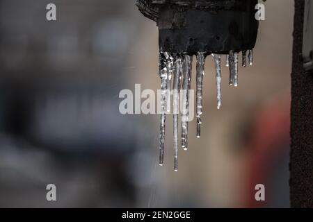 Icules formant des stalactites de glace tombant sur le bord du avant--toits de gouttières avec gouttelettes qui s'écoulent dans un bâtiment résidentiel pendant un hiver froid af Banque D'Images