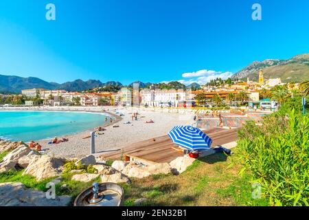 Les touristes et les habitants profitez d'une journée ensoleillée sur la côte d'Azur comme ils vous détendre sur la plage de sable de plage Méditerranéenne Fossan à Menton, France Banque D'Images