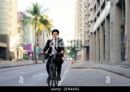 Un homme d'affaires asiatique en costume est à vélo dans les rues de la ville pour se rendre au travail le matin. Concept de transport écologique. Banque D'Images