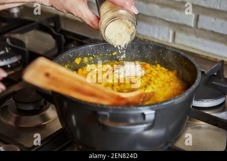 Cuisine à la maison dans la cuisine selon la recette de l'Internet. La femme ajoute du parmesan au risotto dans une poêle. Recette étape par étape. Banque D'Images