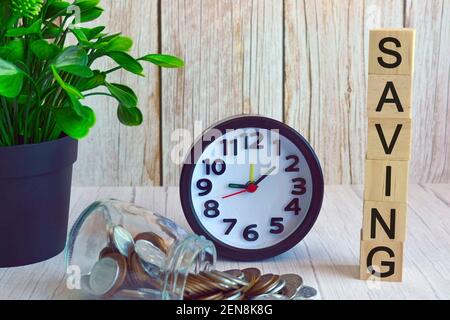 Enregistrement de texte sur un cube en bois avec réveil, plante en pot et pot en verre avec pièces de monnaie sur la surface de la table Banque D'Images