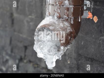 Un tuyau de descente de gouttière gelé. De la glace à l'intérieur du bec verseur, dans le tuyau d'une gouttière de toit près de la fondation de la maison causant des dommages aux gouttières et au toit. Banque D'Images