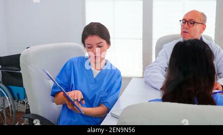 Une infirmière féminine tient un presse-papiers expliquant le diagnostic du patient devant les experts en médecine pendant le séminaire. Thérapeute en clinique parlant avec des collègues de la maladie, professionnel de la médecine Banque D'Images