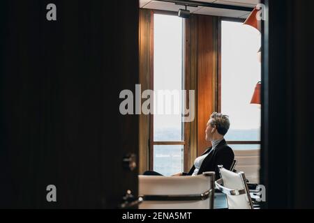 Femme d'affaires attentionnés regardant par la fenêtre, assise dans la salle de conseil vue de la porte Banque D'Images