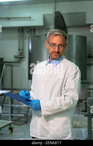 Technologue d'usine laitière avec presse-papiers Vérification du processus de production du fromage. Banque D'Images