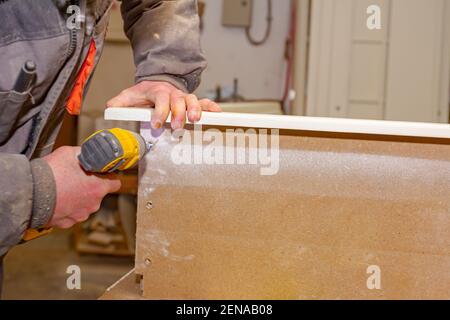Le travailleur en charpenterie utilise un outil électrique manuel professionnel, un foret acu, et tord les vis sur le cadre de porte en bois. Banque D'Images
