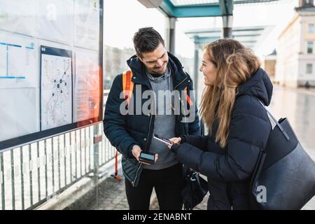 Femme souriante qui scanne le code QR avec un smartphone en position debout homme à la gare Banque D'Images