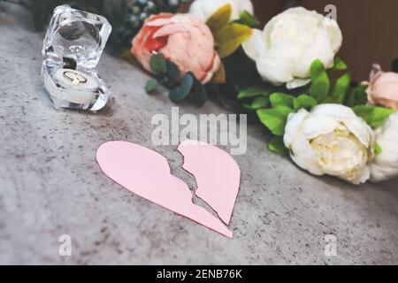 coeur rose déchiré sur la table à côté de la boîte des anneaux de mariage et des fleurs. concept de divorce, séparation, infidélité, rupture de l'engagement . Banque D'Images