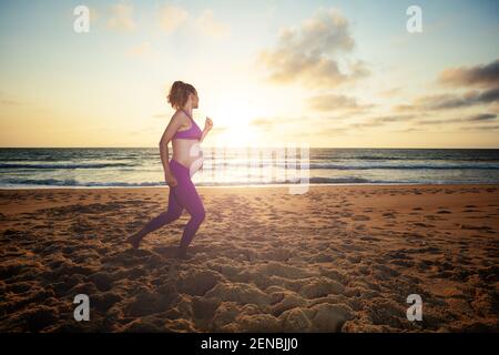 Femme enceinte qui fait du jogging sur la plage au coucher du soleil Banque D'Images