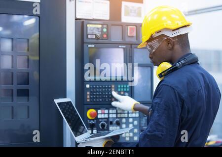 Homme de travail avec casque jaune et clavier de saisie avec protection auditive de l'ordinateur portable en usine Banque D'Images