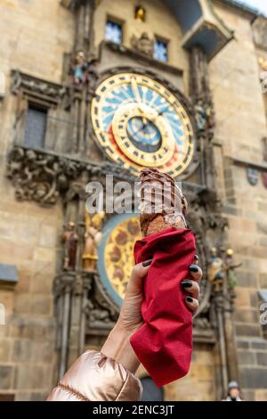 La main féminine tient le cookie tchèque traditionnel trdelnik sur fond d'horloge astronomique dans la vieille ville de Prague. Banque D'Images