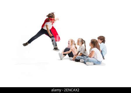 Vol. Enfant prétendant être un super-héros avec ses amis assis autour de lui. Les enfants sont excités et inspirés par leur ami courageux dans un manteau rouge isolé sur fond blanc. Rêves, émotions concept. Banque D'Images