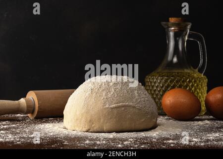 Pâte fraîche brute pour pain ou pizza avec œufs et huile sur une table en bois sombre. Banque D'Images