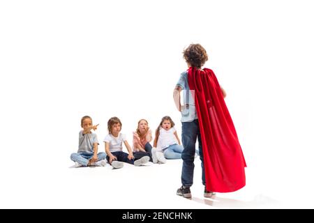 Puissance. Enfant prétendant être un super-héros avec ses amis assis autour de lui. Les enfants sont excités, inspirés par leur forte amie en robe rouge isolée sur fond blanc. Rêves, émotions concept. Banque D'Images