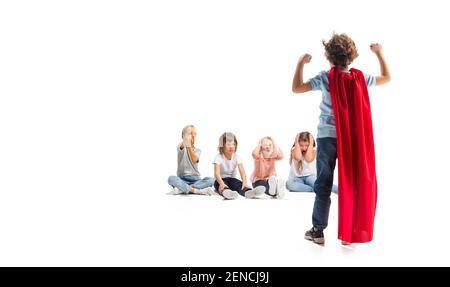 Puissance. Enfant prétendant être un super-héros avec ses amis assis autour de lui. Les enfants sont excités, inspirés par leur forte amie en robe rouge isolée sur fond blanc. Rêves, émotions concept. Banque D'Images