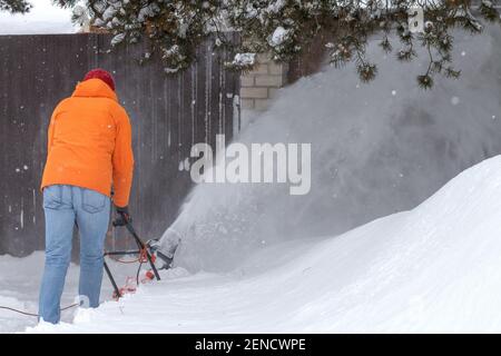 un homme adulte a tiré depuis le dos pour enlever la neige avec un souffleur spécial. Équipement de déneigement avec cordon. Pousser un outil pour nettoyer un trottoir. Un processus de déneigement. Grande vague de neige Banque D'Images