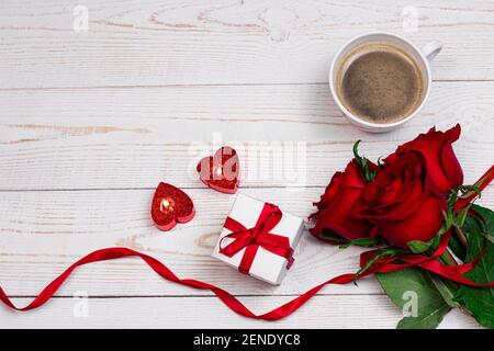 Saint-Valentin romantique petit déjeuner plat fond. Tasse de café bougies en forme de coeur avec boîte cadeau et roses rouges sur fond blanc en bois. Banque D'Images