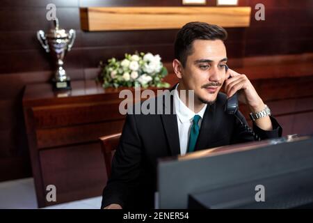 Un réceptionniste qui travaille dur à parler au téléphone et à gérer les souhaits des clients Banque D'Images