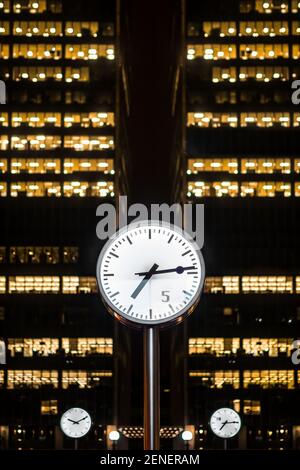 Canary Wharf, Londres 29 octobre 2020 grandes horloges en acier inoxydable montrant du temps avec des gratte-ciel debout derrière les fenêtres de nuit illuminées dans la nuit Banque D'Images