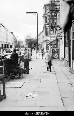 Royaume-Uni, West London, Notting Hill, 1973. Les grandes maisons de quatre étages en ruine et en ruine commencent à être restaurées et redécorées. Kensington Park Road sur la droite à la blanchisserie. Boutiques sur le croissant Elgin et réparations de la chaussée. Banque D'Images