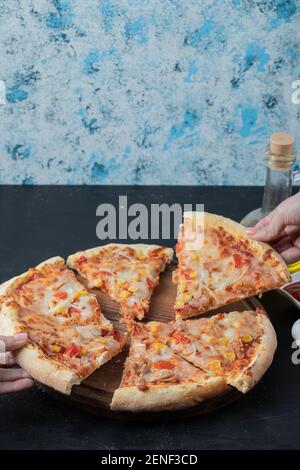 Pizza chaude en tranches. Une femelle prend une tranche de pizza à la main Banque D'Images