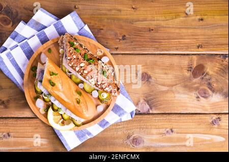 Hareng hollandais dans un sandwich de pain de céréales sur fond de bois d'en haut. Griller avec du hareng hollandais, des oignons et des cornichons. Hors-d'œuvre rustique traditionnel avec fruits de mer. Nourriture aux pays-Bas. Copier l'espace Banque D'Images