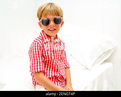 Portrait d'un enfant souriant dans une chemise à carreaux et avec des lunettes de soleil sur un fond clair. Pendant les vacances d'été. Banque D'Images