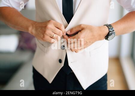 Un homme soutenant le gilet de son costume dans un chambre d'hôtel lors de la préparation d'une cérémonie de mariage Banque D'Images