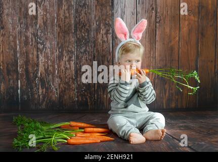 Mignon jeune garçon dans les oreilles de lapin mâchant sur un carotte Banque D'Images