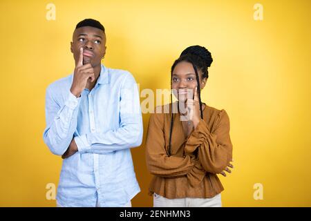 Jeune couple afro-américain debout sur fond jaune avec la main sur le menton pensant à la question, l'expression pensive. Souriant et pensive fa Banque D'Images