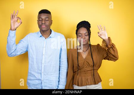 Un jeune couple afro-américain debout sur fond jaune se détend et souriant avec les yeux fermés faisant un geste de méditation avec les doigts Banque D'Images