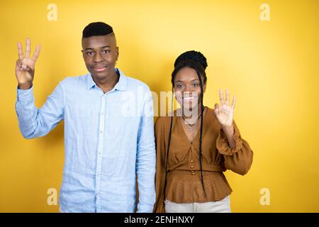Jeune couple afro-américain debout sur fond jaune montrant et pointant vers le haut avec les doigts numéro trois tout en souriant confiant et heureux Banque D'Images