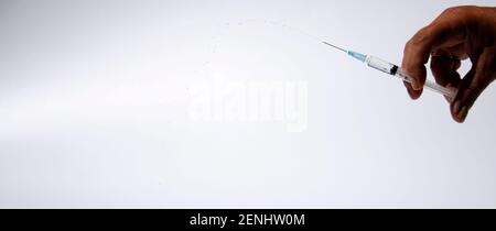 Main isolée avec seringue et gouttes filés dans l'air. Beaucoup d'espace de copie sur le côté gauche Banque D'Images
