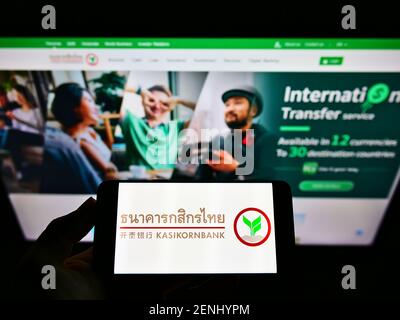 Personne tenant un smartphone avec le logo de la banque thaïlandaise Kasikornbank PCL (KBank) à l'écran devant le site Web. Mise au point sur l'affichage du téléphone. Photo non modifiée. Banque D'Images