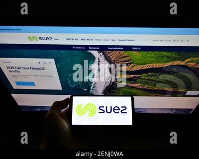 Personne tenant un smartphone avec le logo de la société de services publics française Suez S.A. à l'écran devant le site Web. Mise au point sur l'affichage du téléphone. Photo non modifiée. Banque D'Images