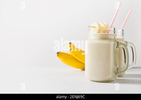 Deux milkshakes de banane sains dans un pot de maçon sur blanc. Boisson végétalienne savoureuse. Gros plan. Copier l'espace. Banque D'Images